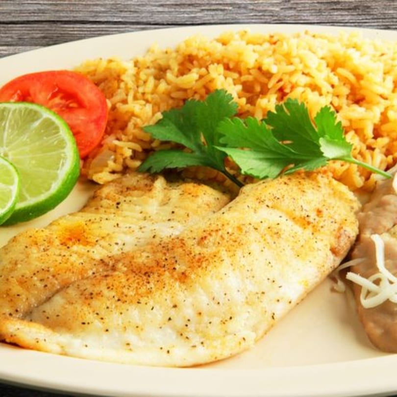 Grilled fish fillet with Mexican rice, refried beans, lime, tomato, and cilantro on a plate.