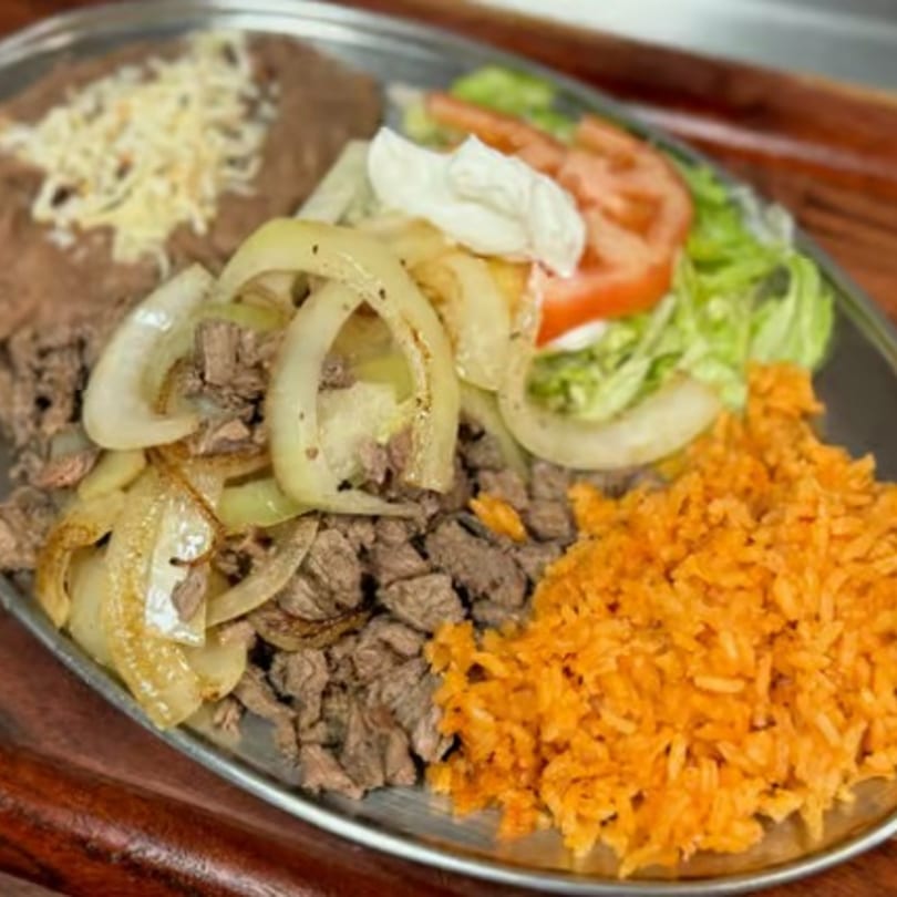 My Taco House's carne asada plate with rice, beans, grilled onions, lettuce, tomato, and sour cream.
