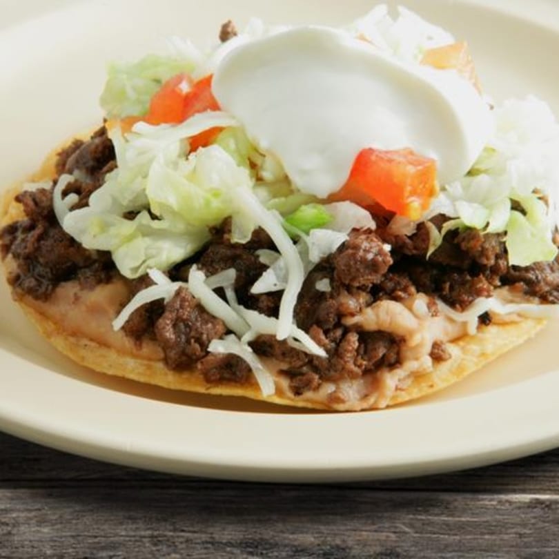 A My Taco House tostada with ground beef, beans, lettuce, tomatoes, and sour cream.